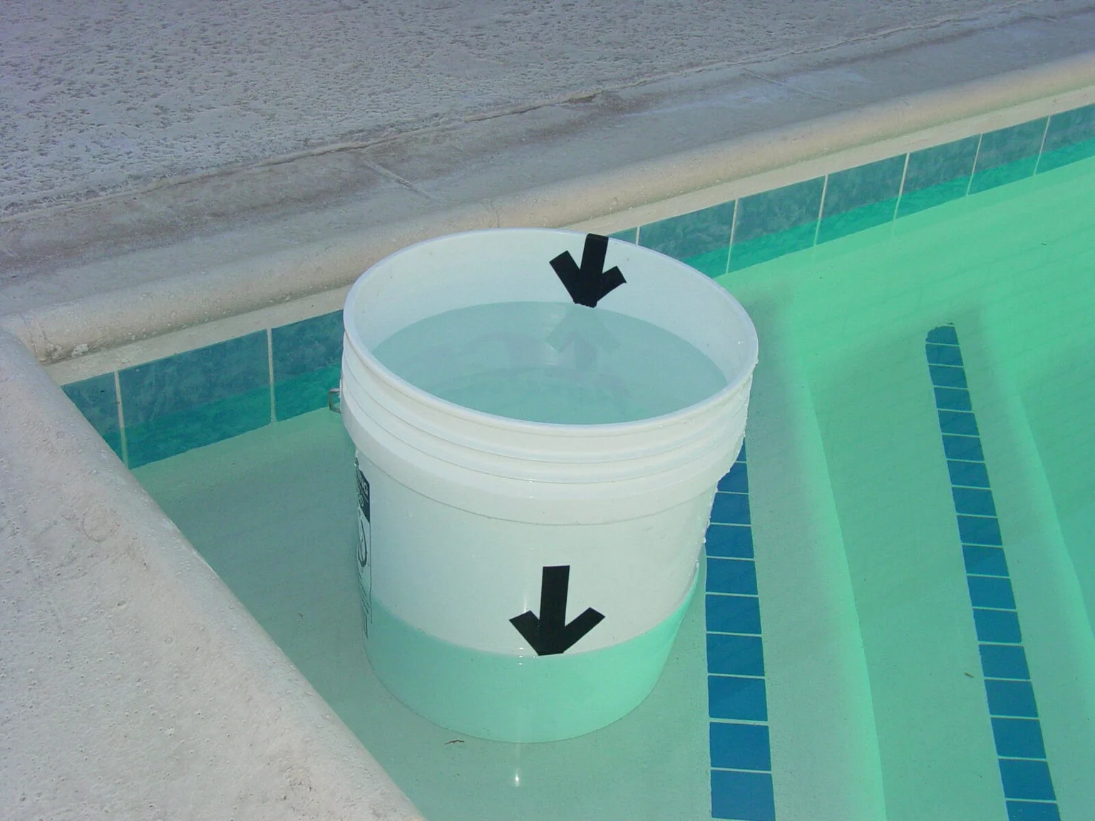 Water-filled bucket sitting on a pool step with inside and outside water-level marks
